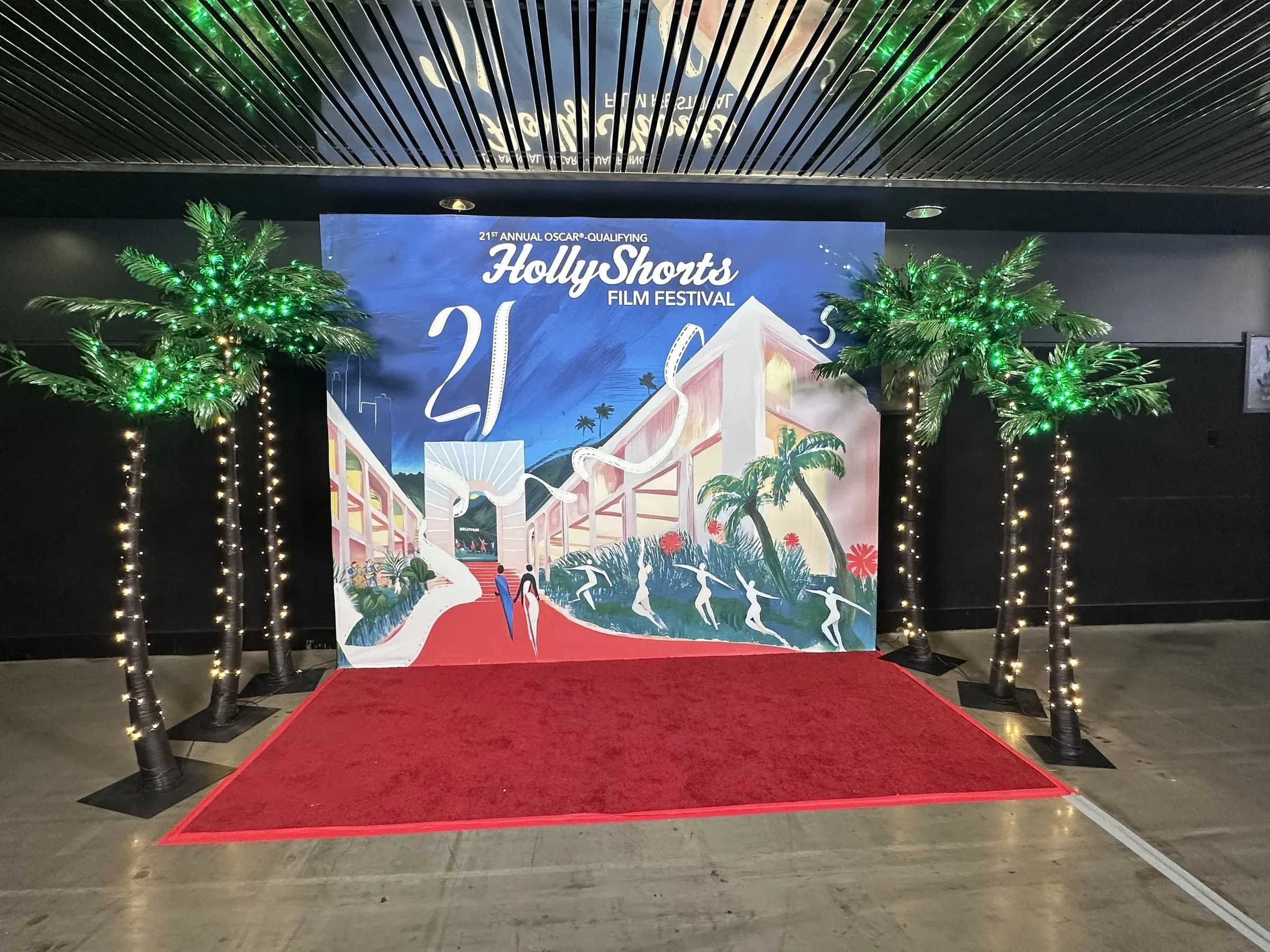 The poster-art backdrop with lit palm trees and a red carpet.