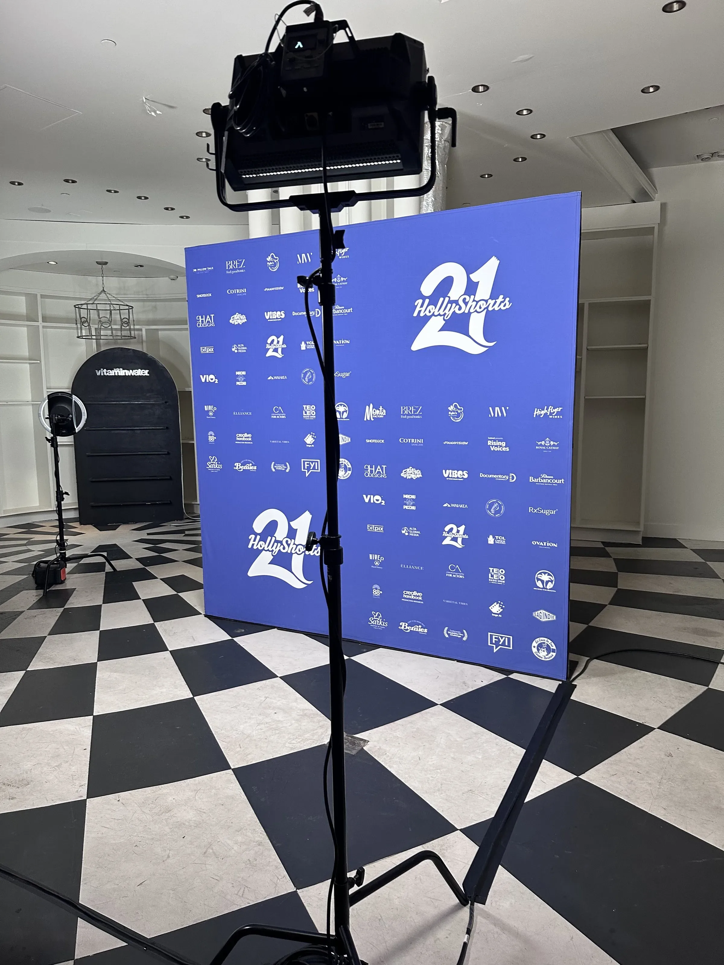 Blue step-and-repeat on a checkered floor with a lighting stand