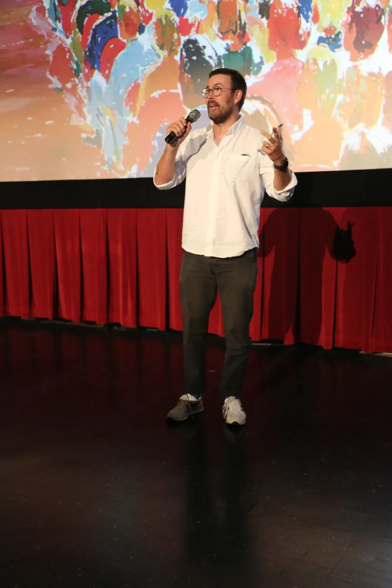 The host on stage in front of the poster art.