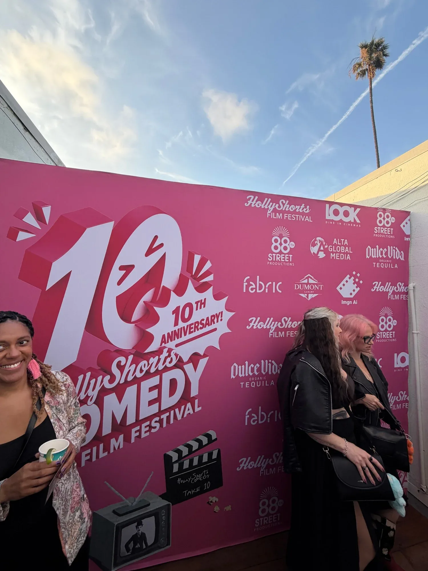 The 10th anniversary step-and-repeat outdoors, under a blue sky and a palm tree