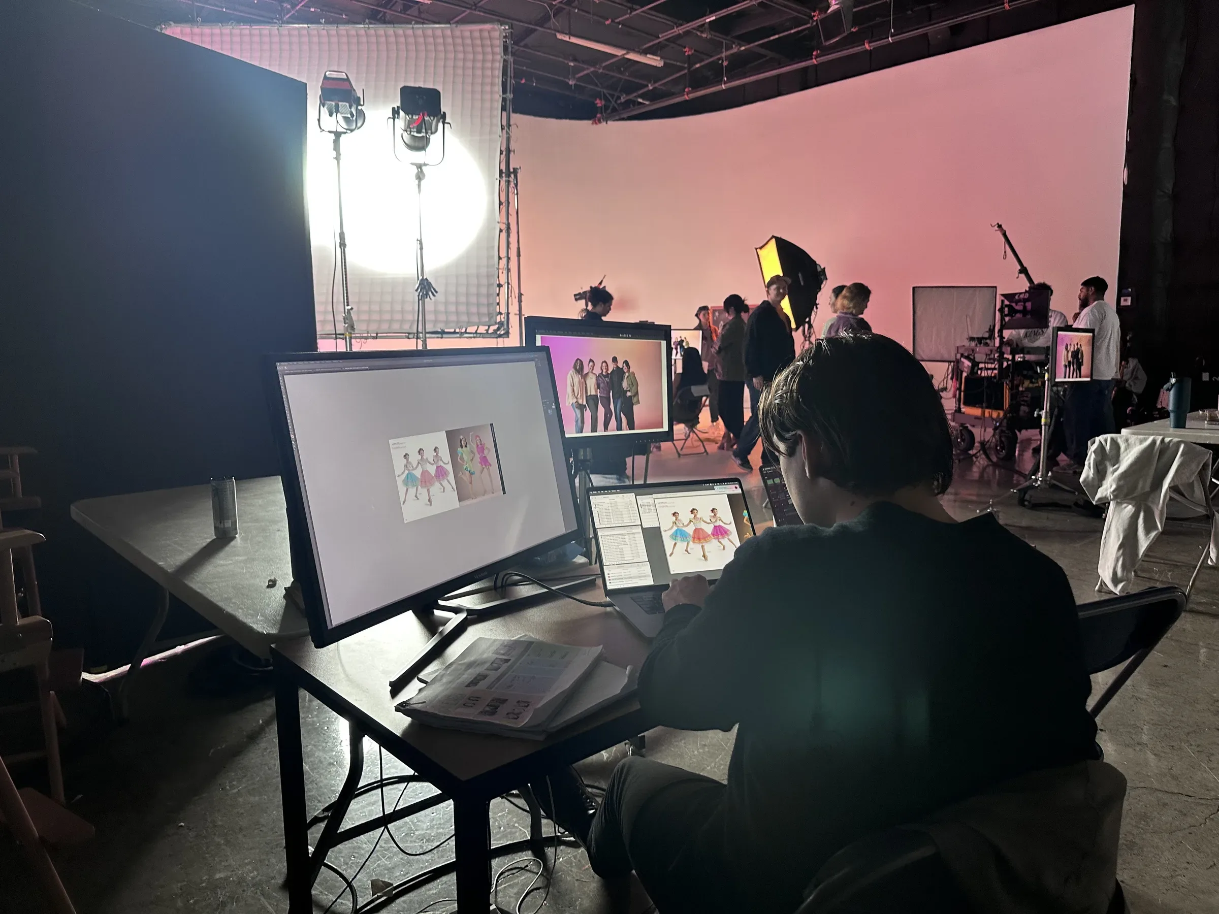 The production desk on set: a multi-screen workstation in front of a pink cyclorama.